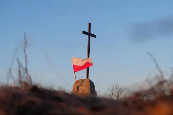 Na kamieniu, pod krzyżem, powiewa biało-czerwona flaga Polski.