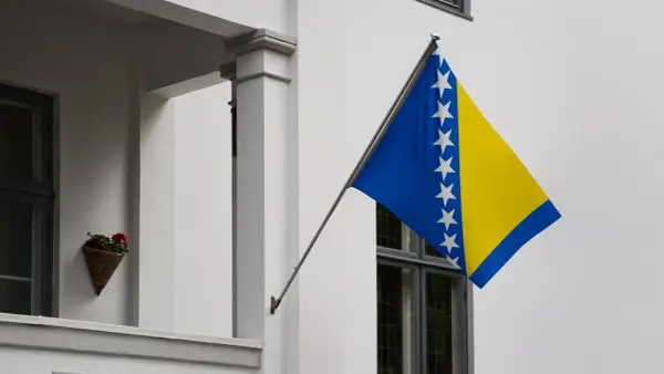Flaga Bośni i Hercegowiny powiewa na tle białej ściany.