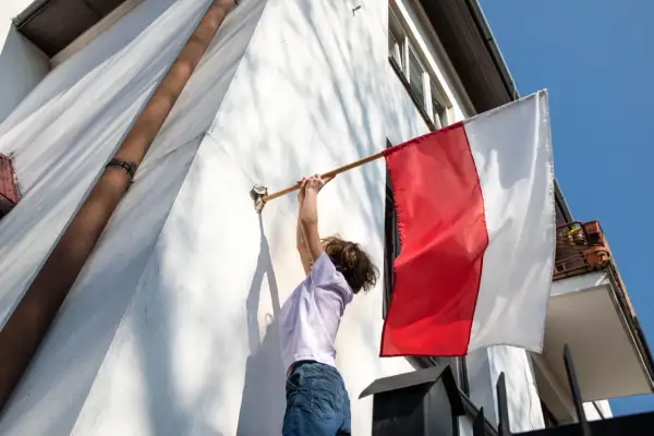 Dziecko zdejmuje biało-czerwoną flagę. Zgodnie z tradycją, flagę zdejmuje się po 3 maja, gdy minie czas jej wywieszenia.