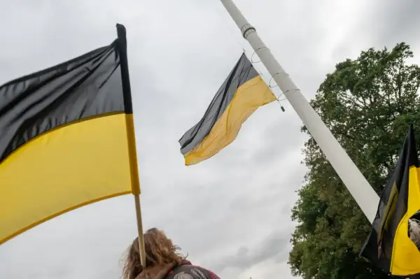 Flaga Kaszub powiewa na maszcie. Dwie flagi w kolorach czarnym i żółtym, symbolizujące Kaszuby, są widoczne na tle pochmurnego nieba.